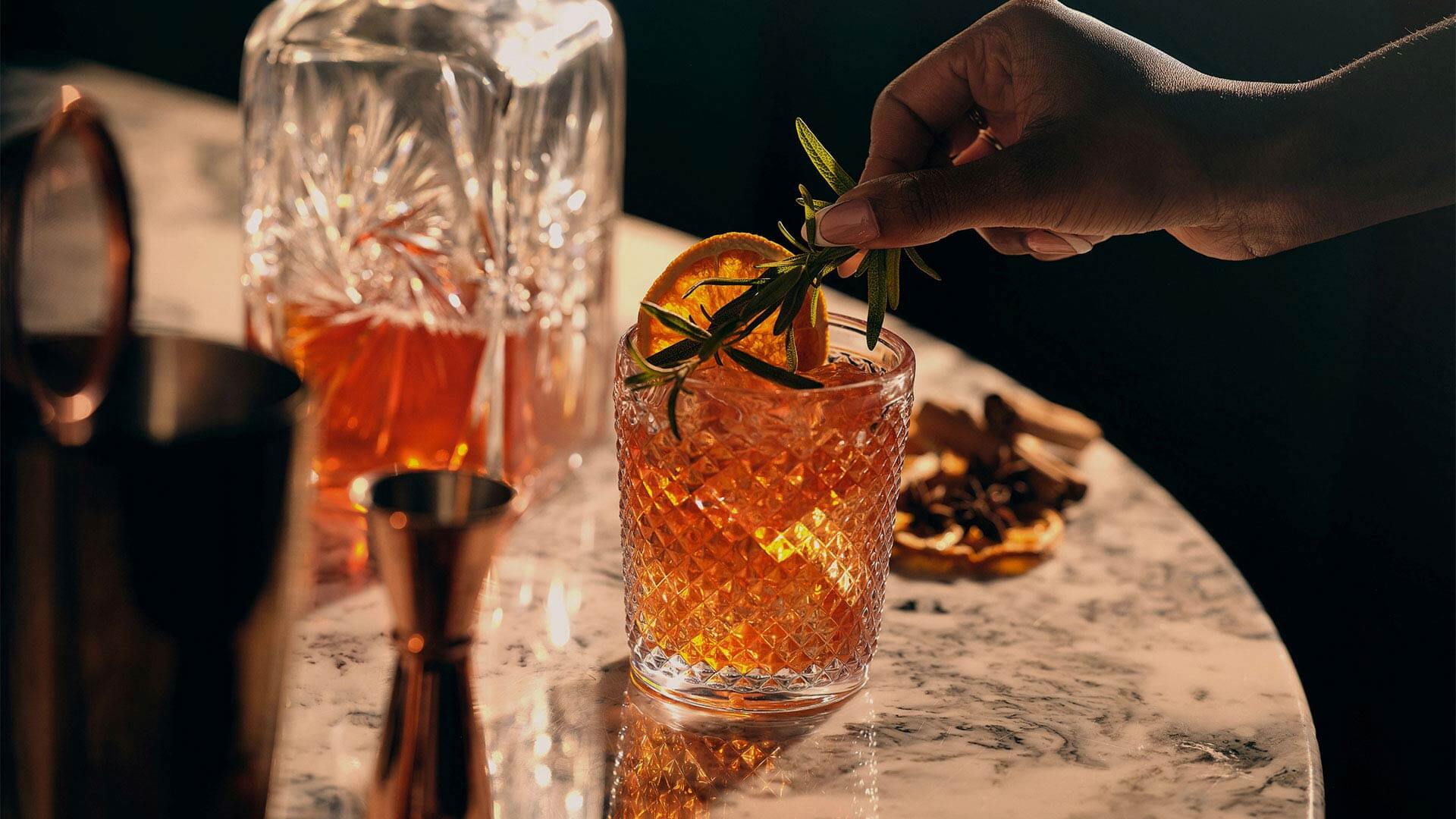 A bartender laying rosemary on an orange old fashioned