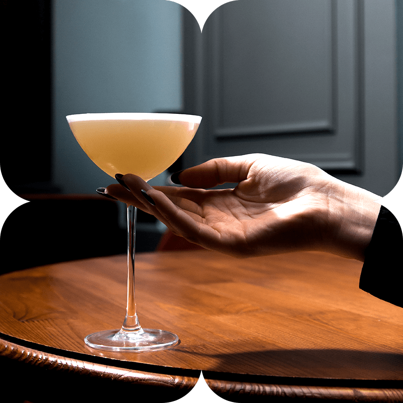 A hand resting a coupe of sour on a walnut table