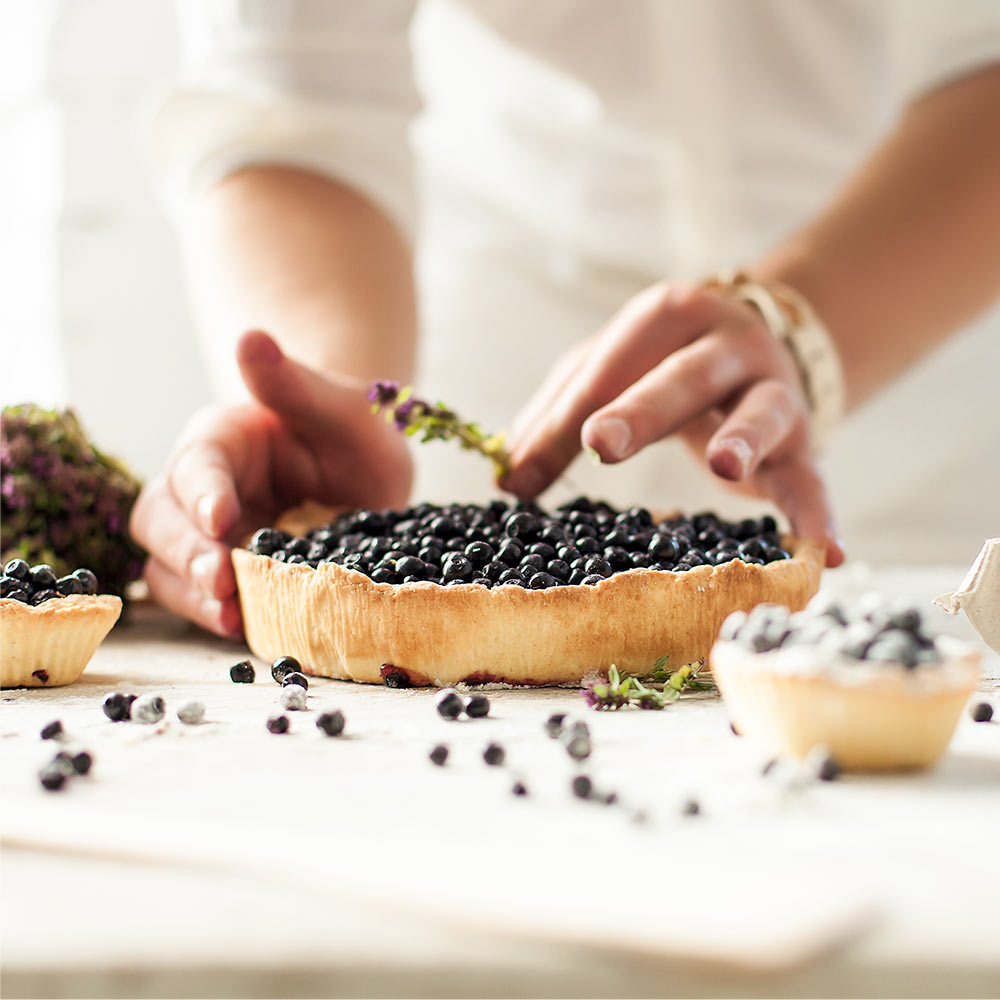 Hands placing blueberries on a tart