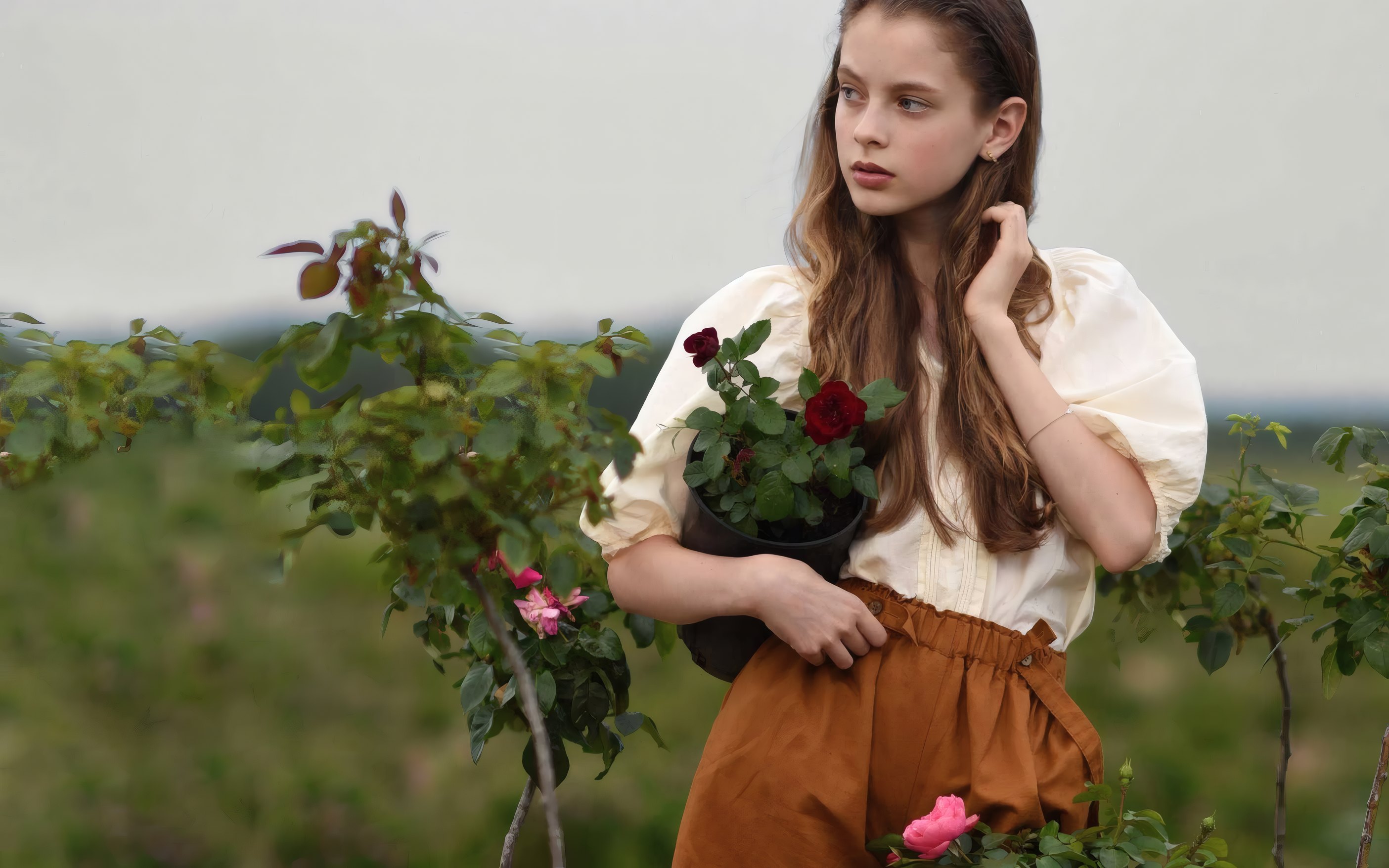 A girl in a puff-sleeve blouse holding a pot of roses in a garden