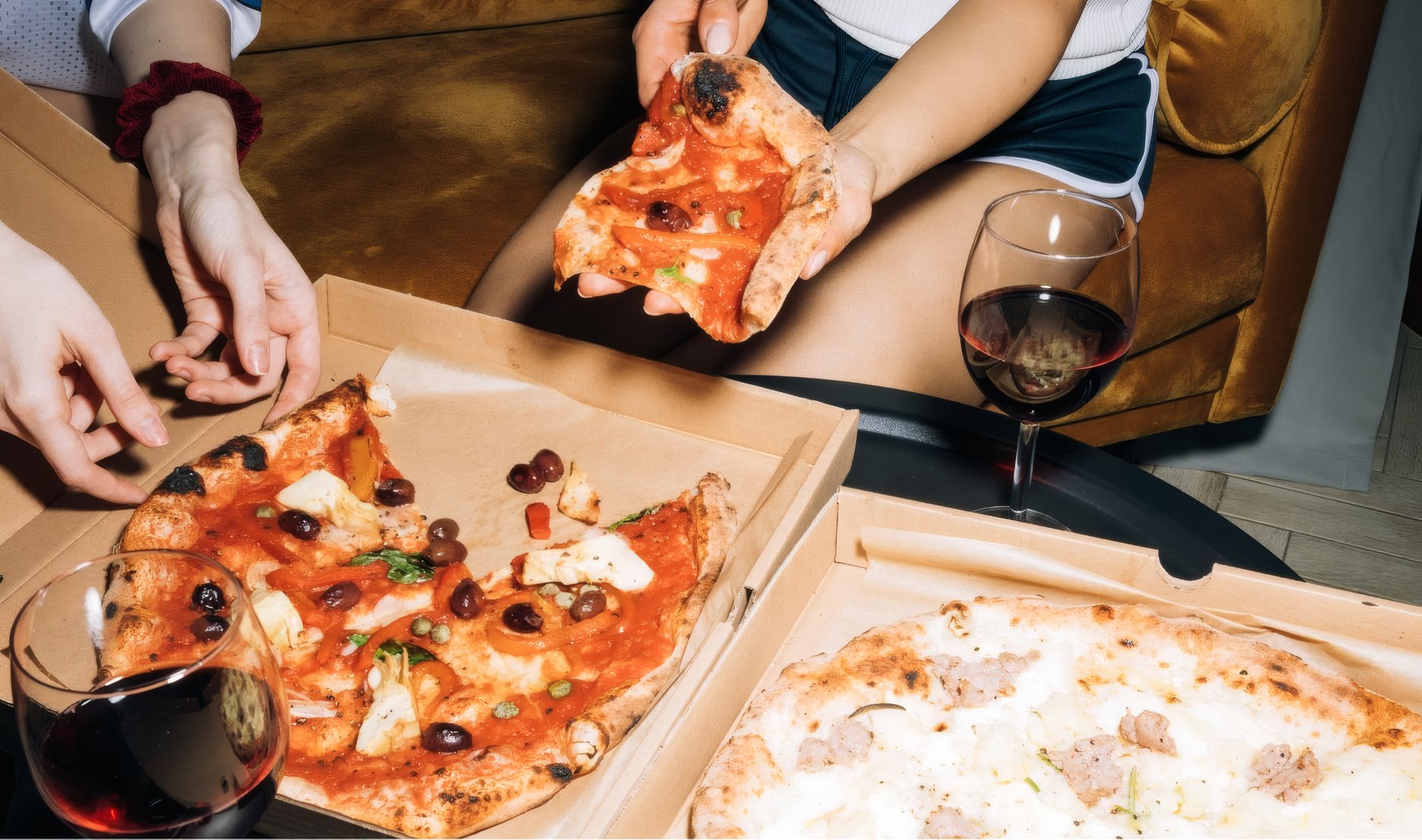 Friends reaching into two open pizza boxes