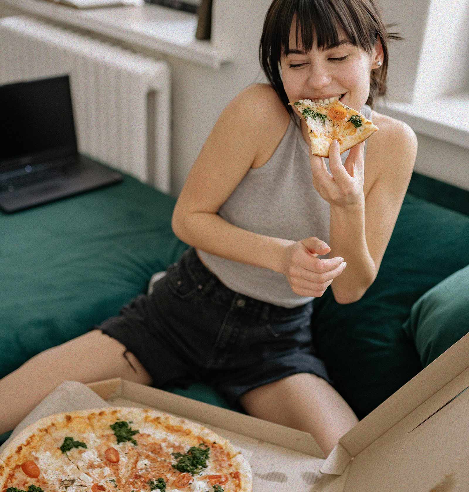 A friend eating a slice on a green sofa, the box open on her knees