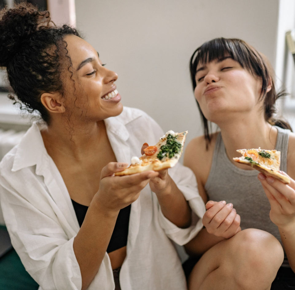 Two friends sharing pizza on a sofa
