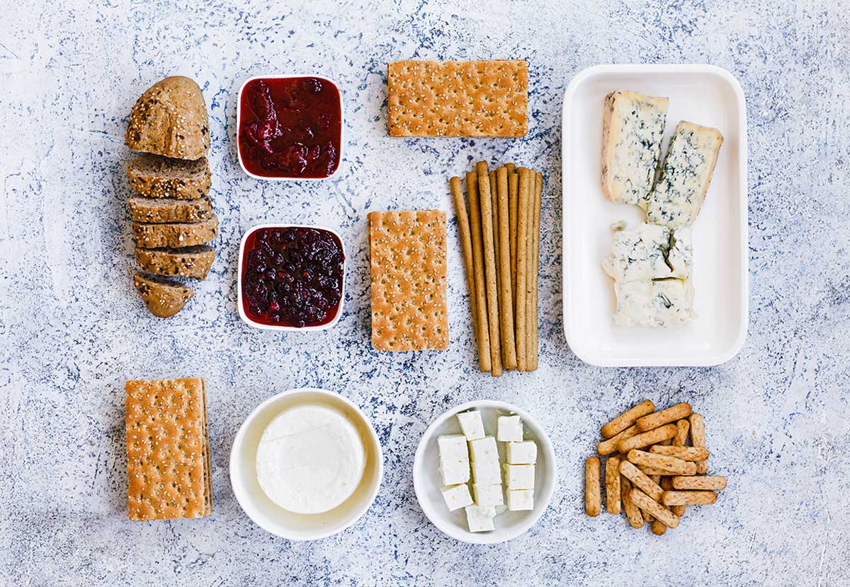 Crackers, jams, cheeses and breadsticks laid out on a grey table