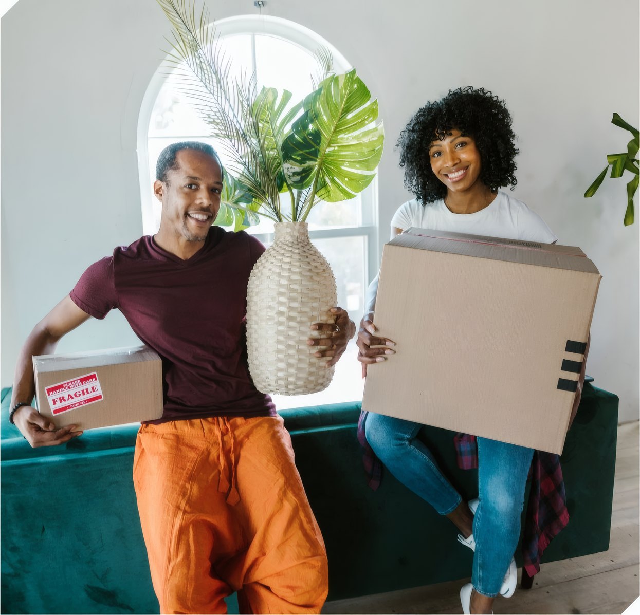 A couple carrying boxes and a plant into their new home