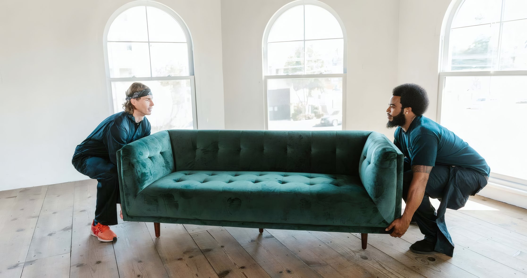Two movers lifting a green velvet sofa