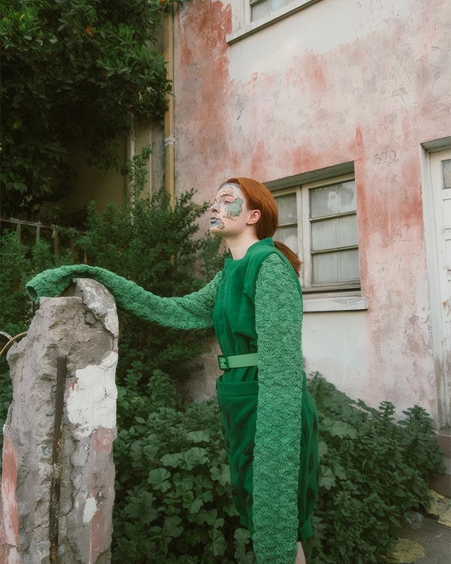A woman in an emerald knit tunic and trousers by a pink wall