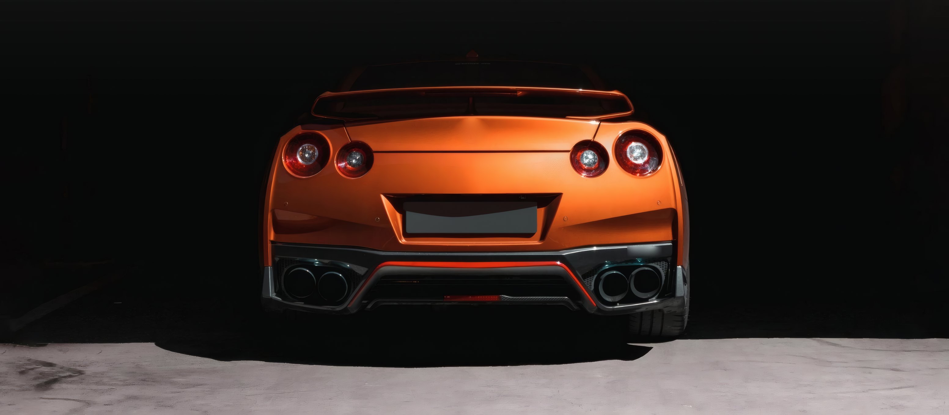 An orange coupe from behind in a black studio