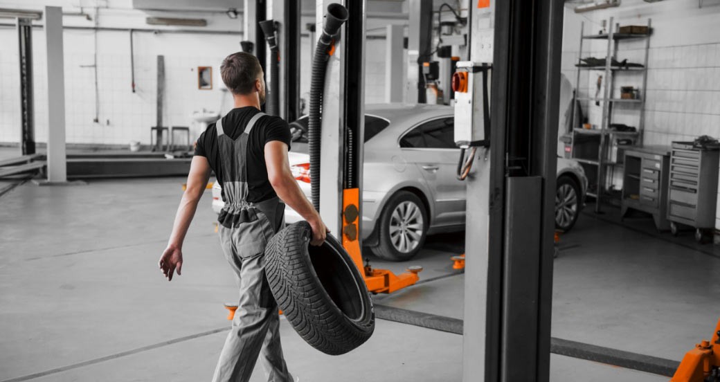 A technician carrying a tyre across the workshop