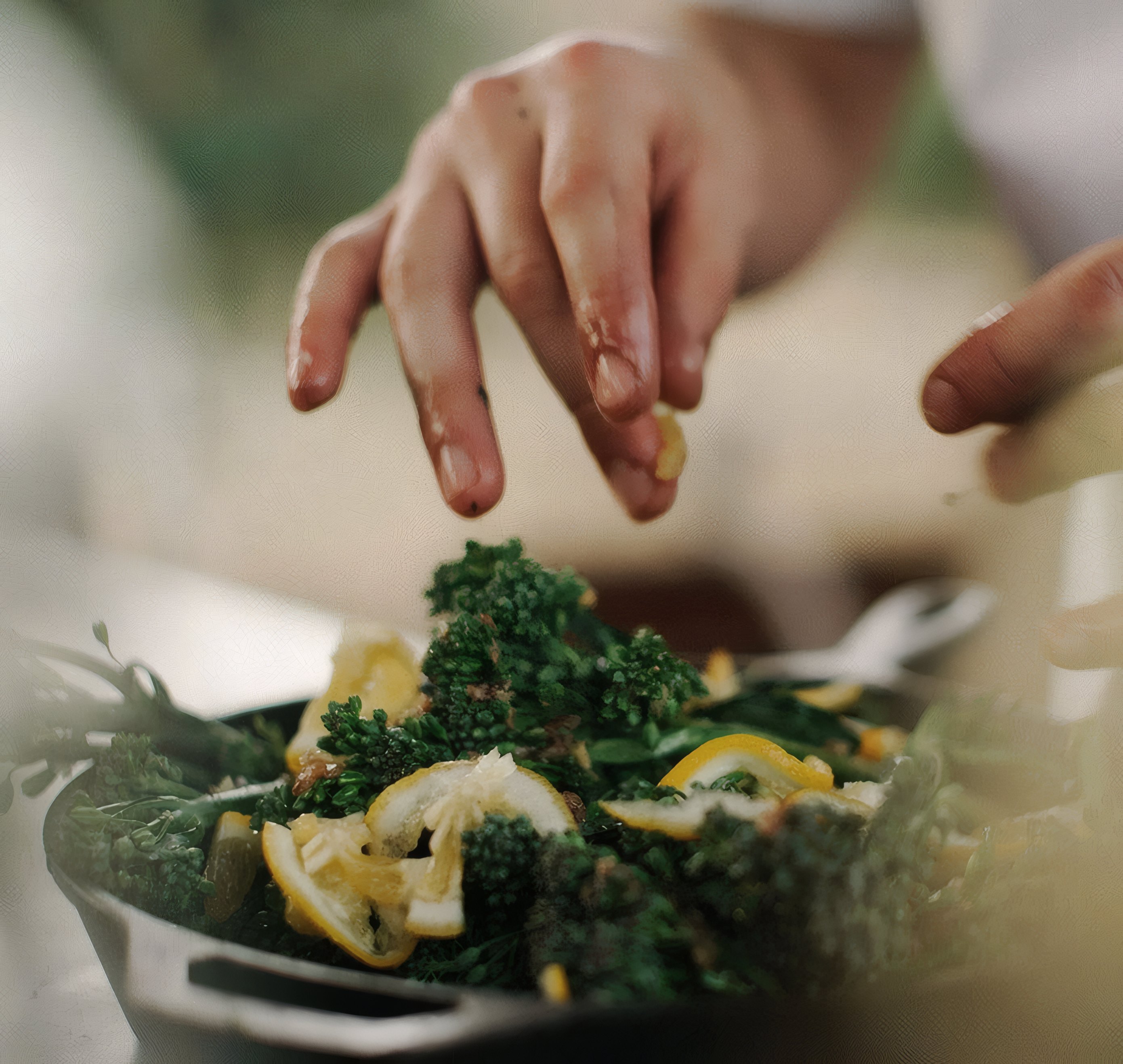 Hands scattering greens over a dish