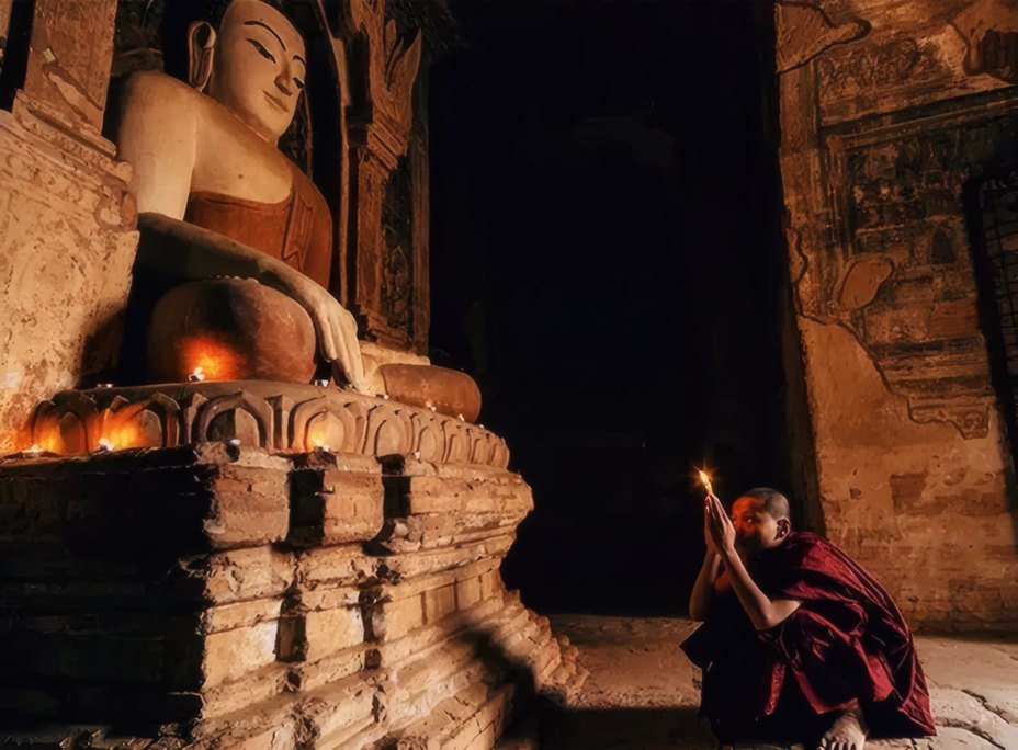 A novice lighting candles beneath a great Buddha
