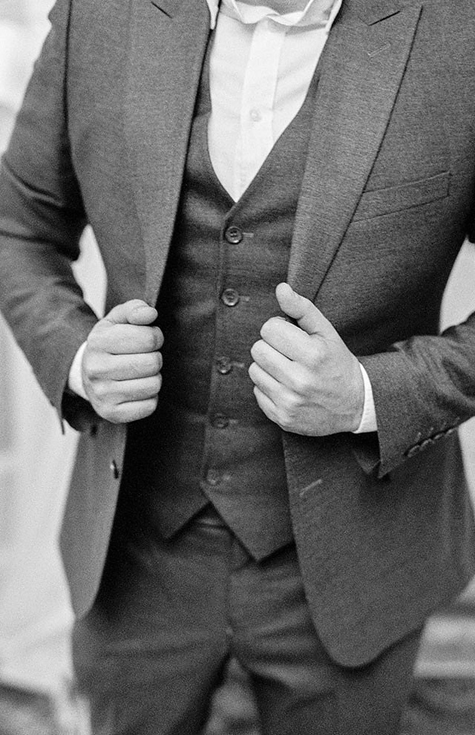A man in a grey three-piece fastening his jacket