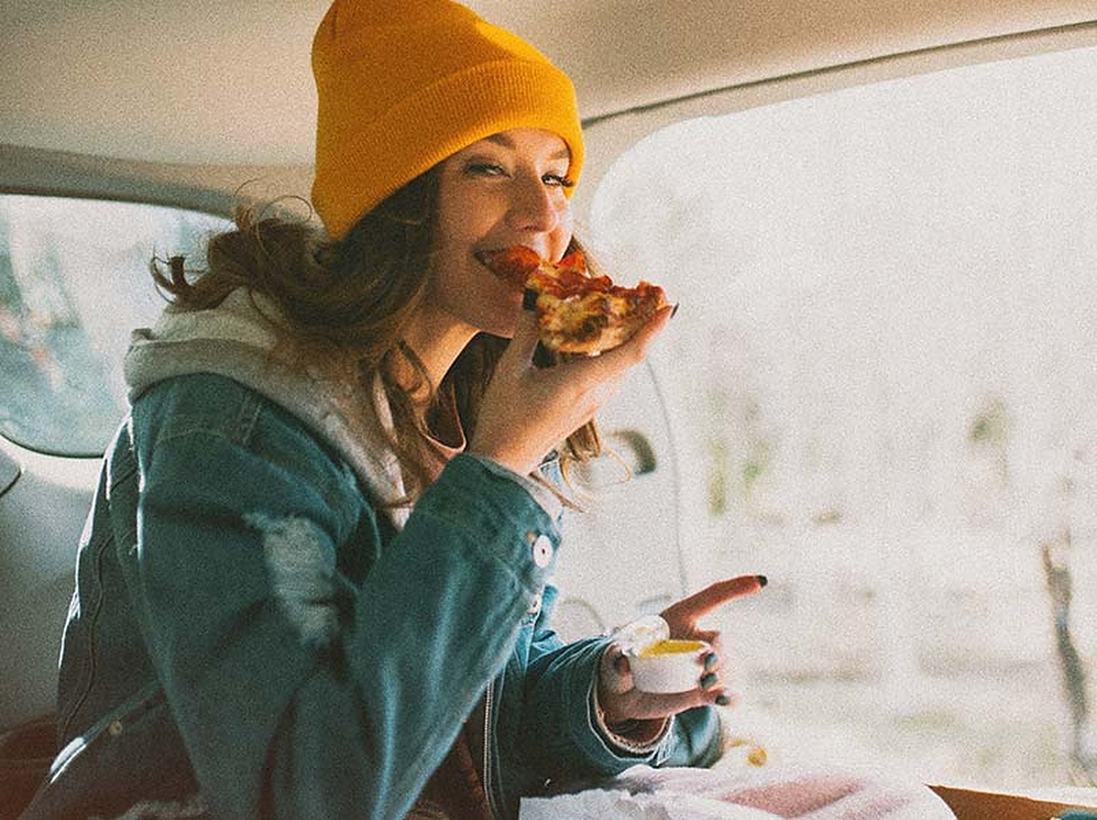 A woman biting into a slice in a car