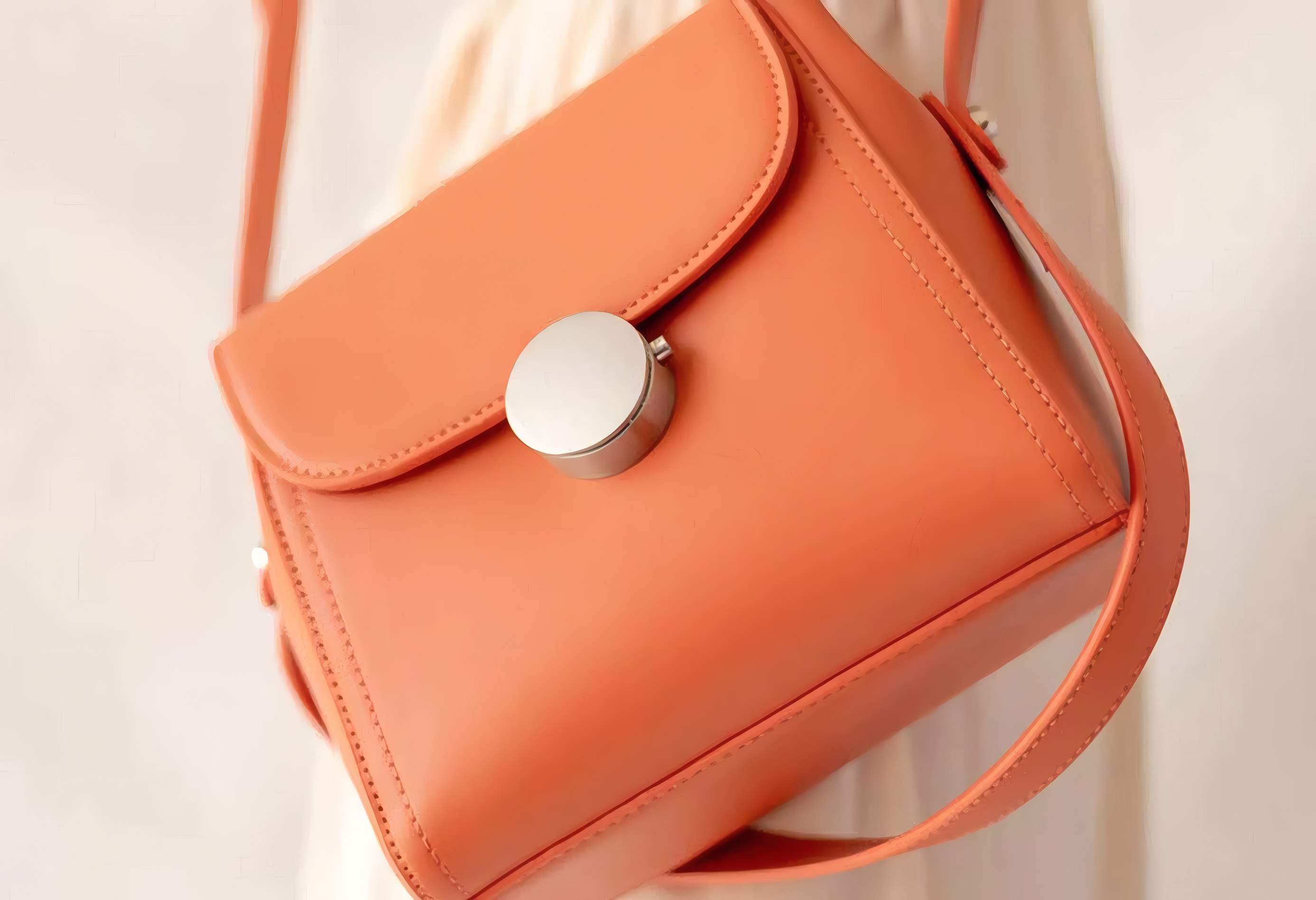 An orange leather crossbody bag against a white summer dress