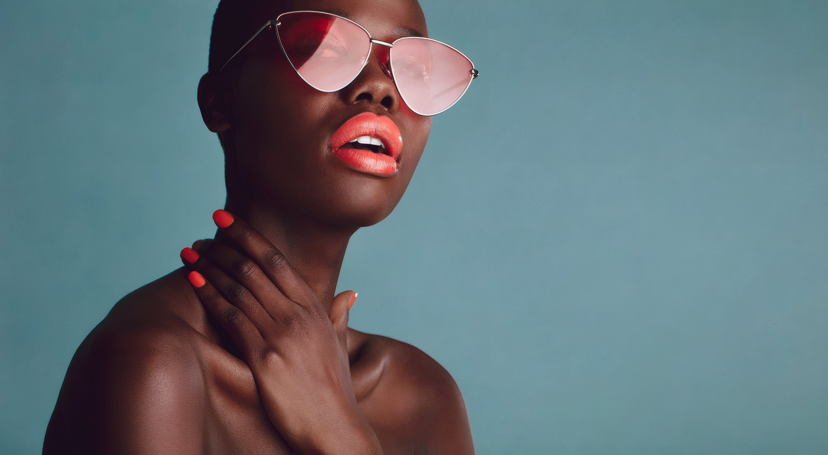 A woman in pink cat-eye sunglasses against a teal wall