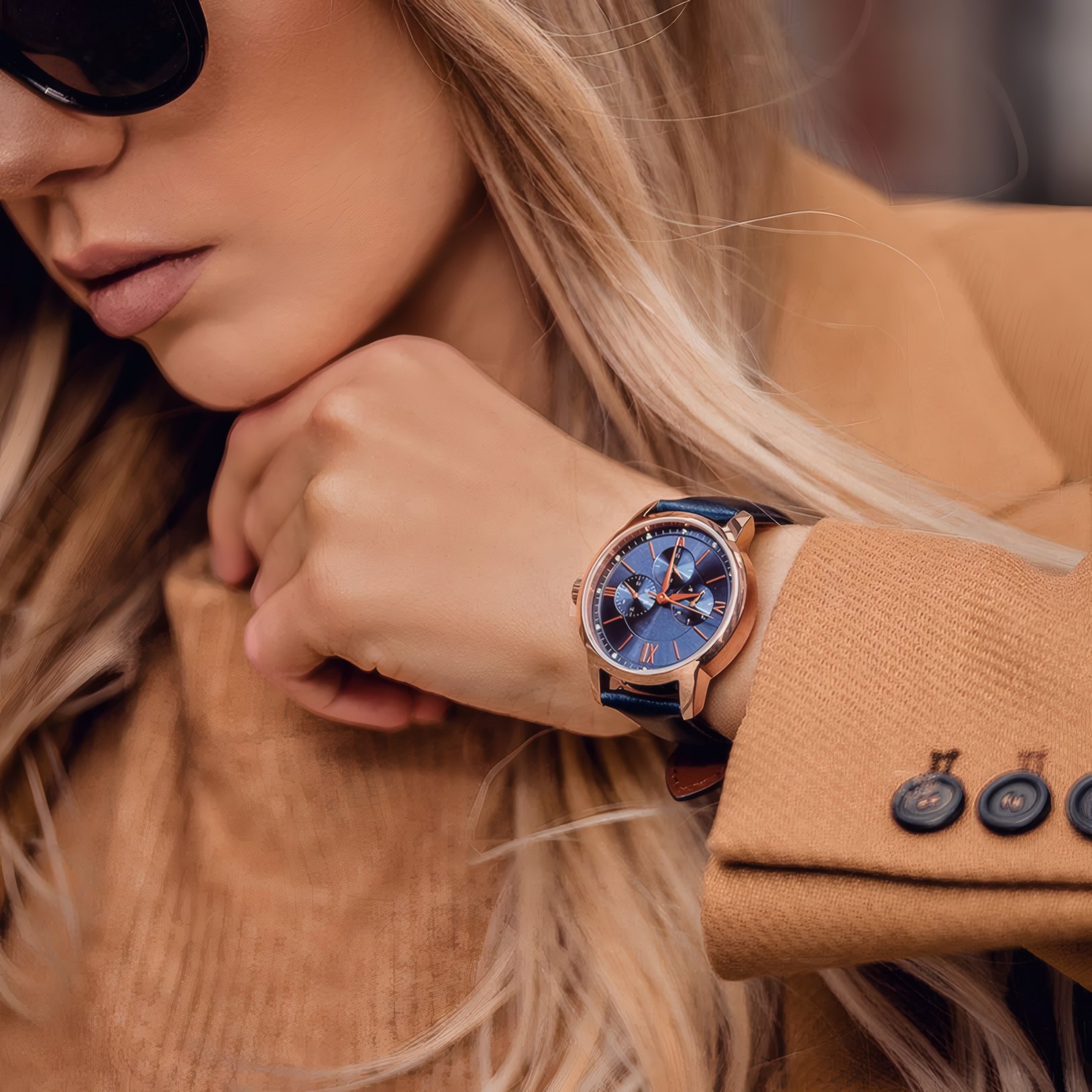 A rose gold watch on a wrist in a camel coat