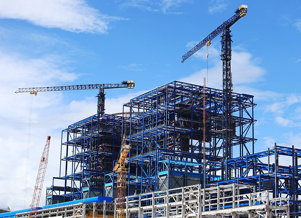 A blue steel frame rising between two tower cranes