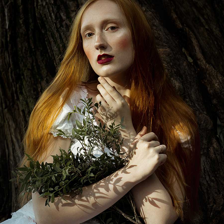 A red-haired woman holding wild herbs against dark leaves