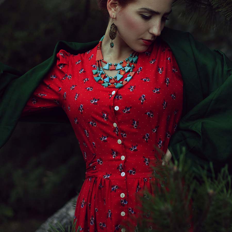 A dark-haired woman in a red dress and a turquoise necklace