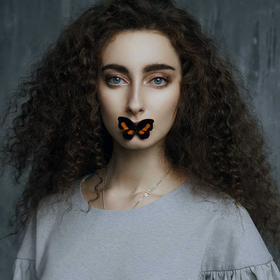 A curly-haired woman with a butterfly over her lips