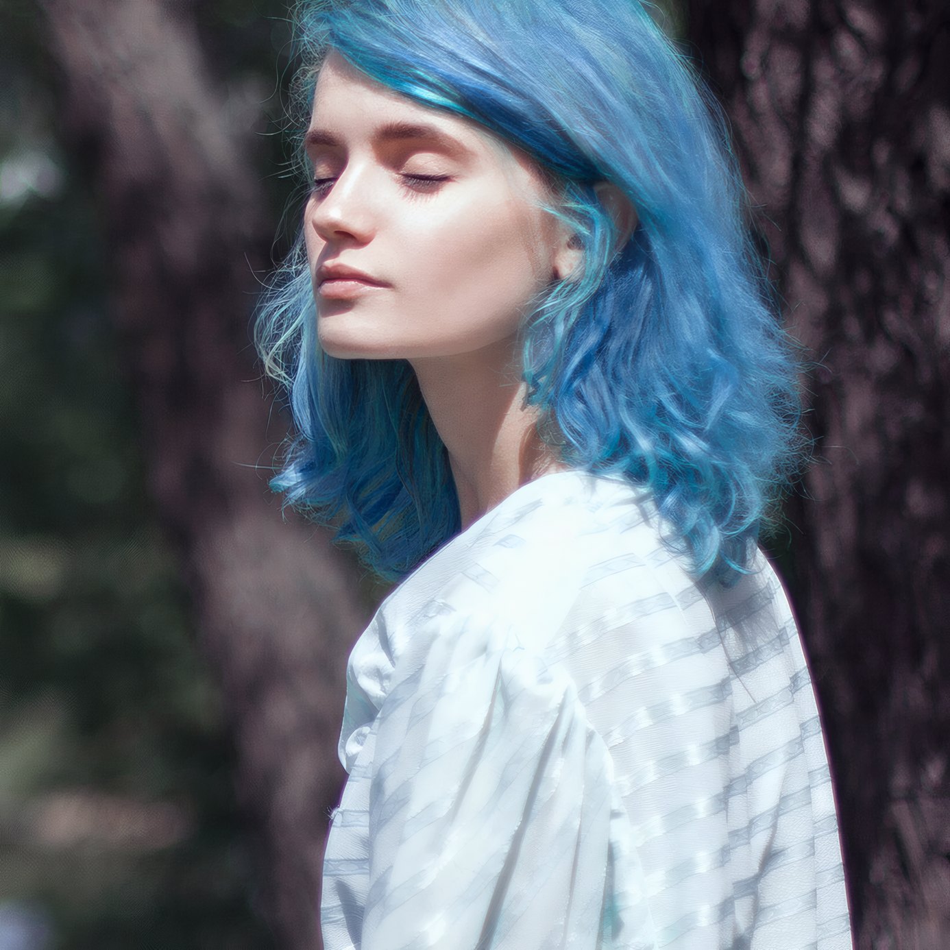 A young woman with blue hair under dark leaves at dusk