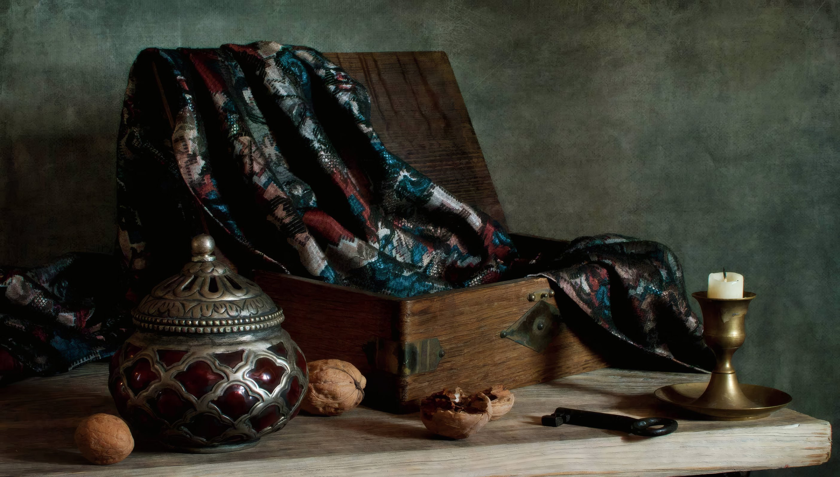 An open wooden box with a patterned carpet spilling out, a brass urn, walnuts and a key