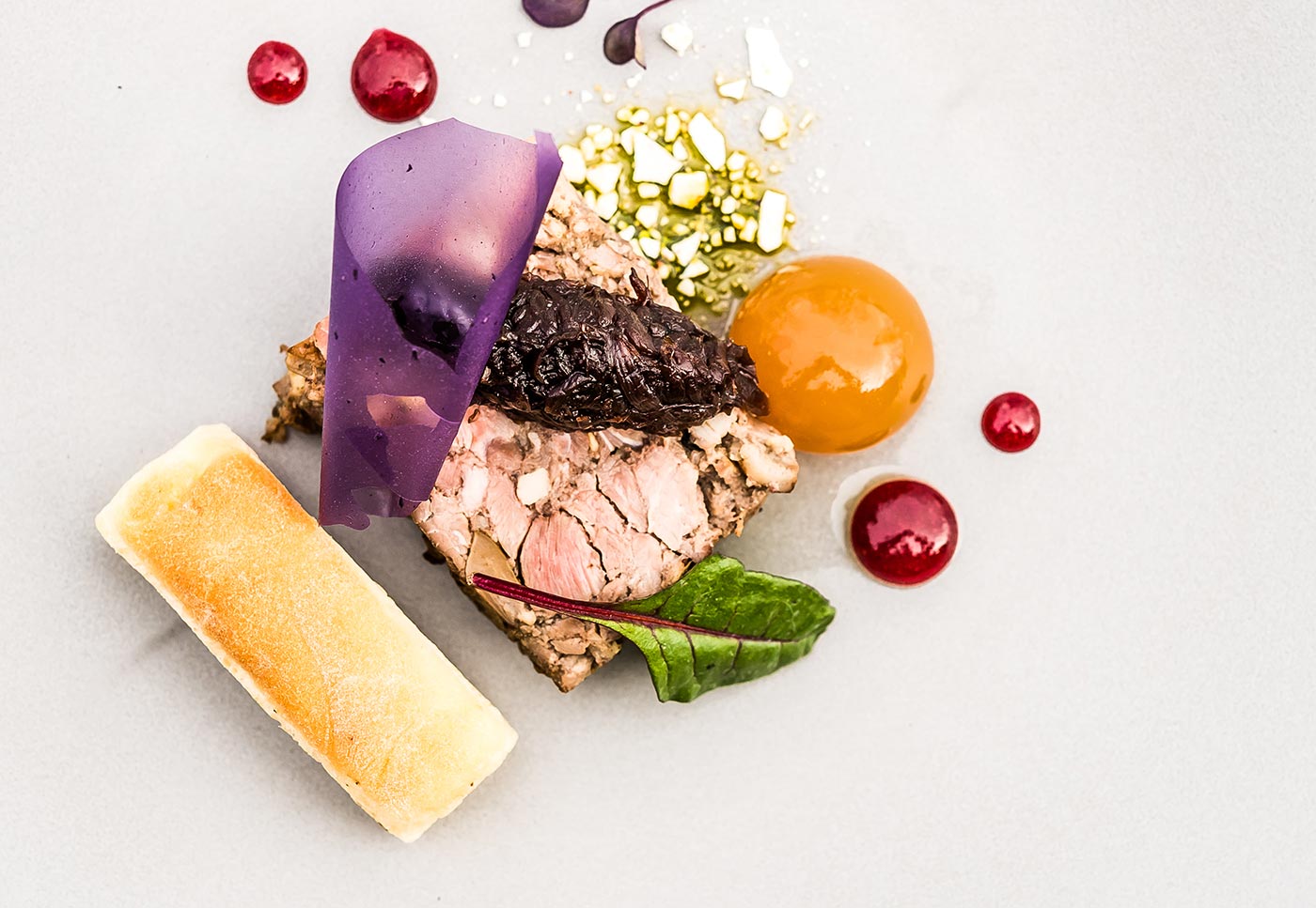 A plated dish of lamb with a purple tuile