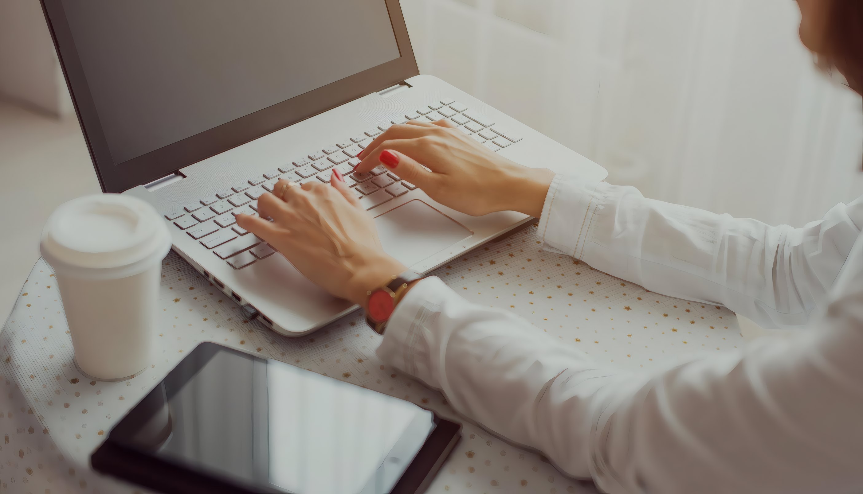 Hands typing on a laptop beside a coffee