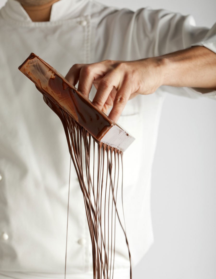 Hands lifting tempered chocolate from a marble slab