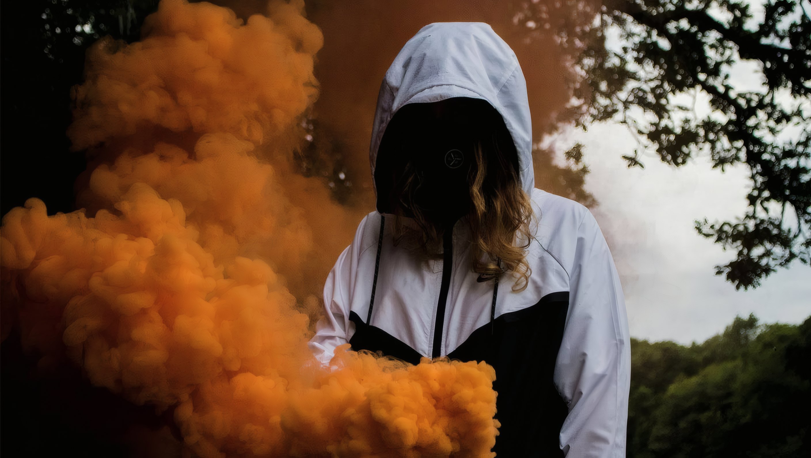 A hooded figure in a cloud of orange smoke