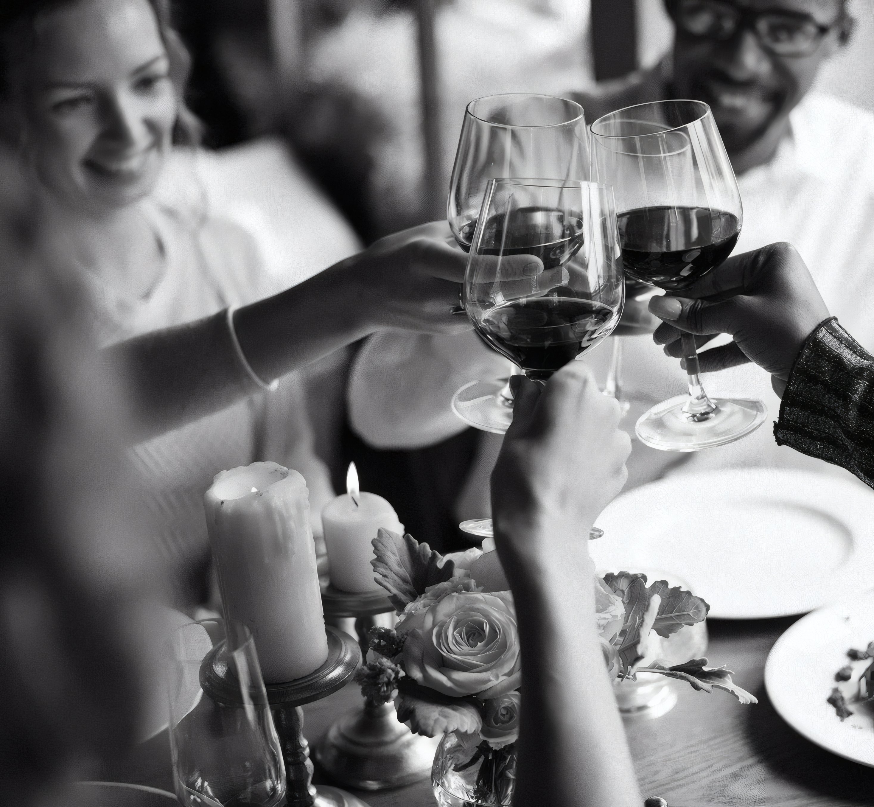 Glasses of red wine raised over a candlelit table