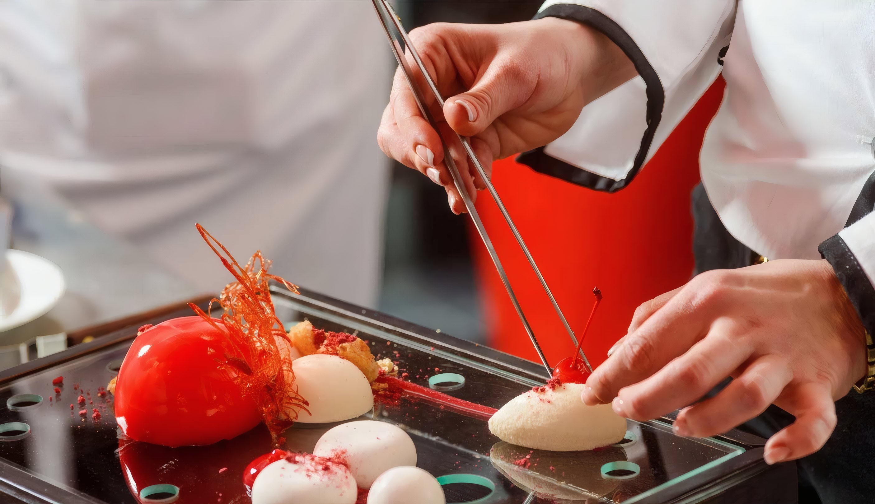 A chef plating a red sphere with tweezers