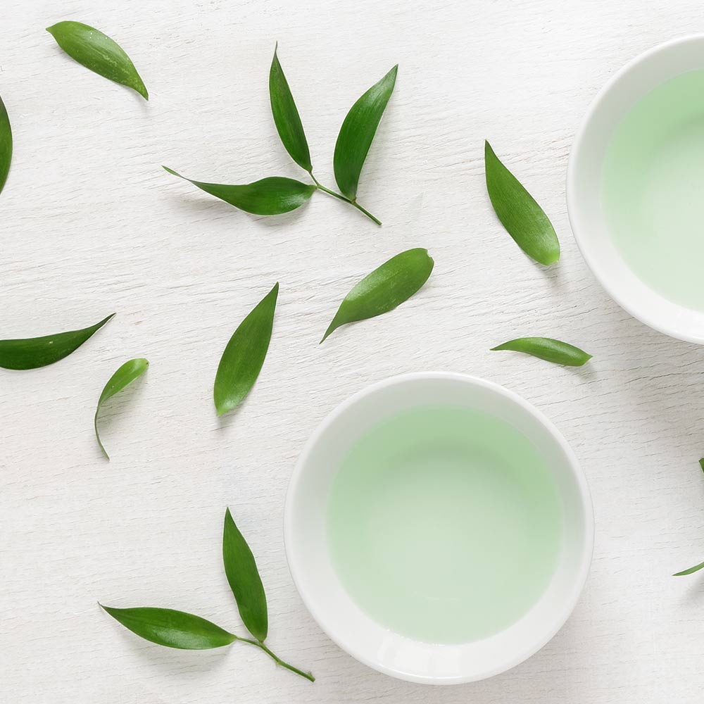 Pale green tea in a white cup among fresh leaves, seen from above