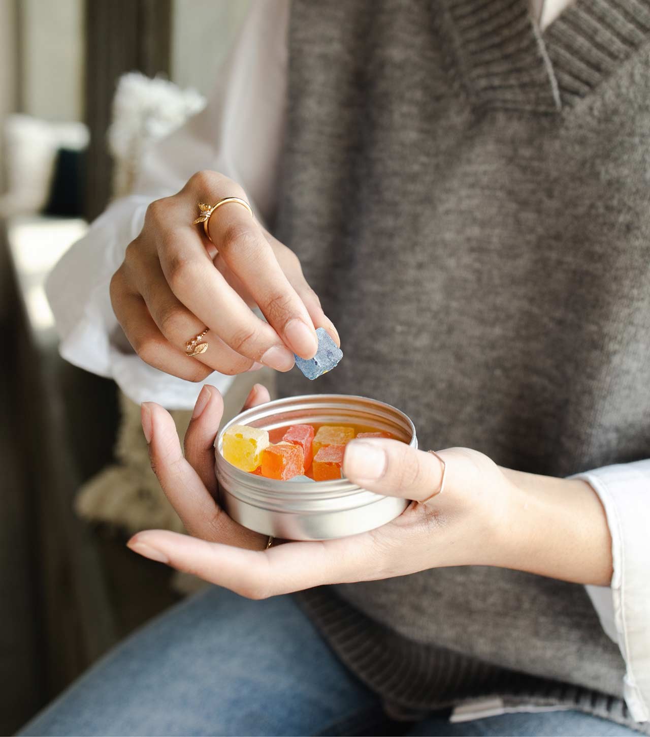 Hands opening a tin of orange and yellow gummies