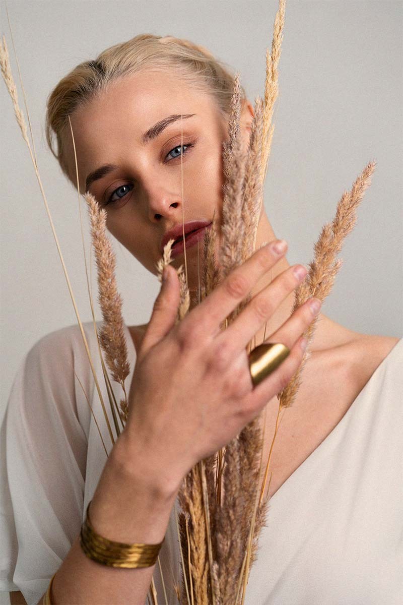 A woman holding dried wheat, a gold ring on her finger