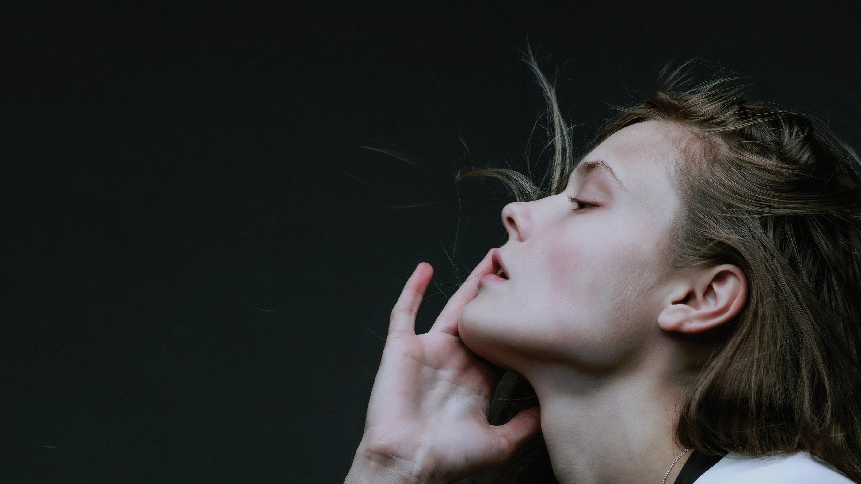 A model in profile, her hand at her jaw, on a dark green ground