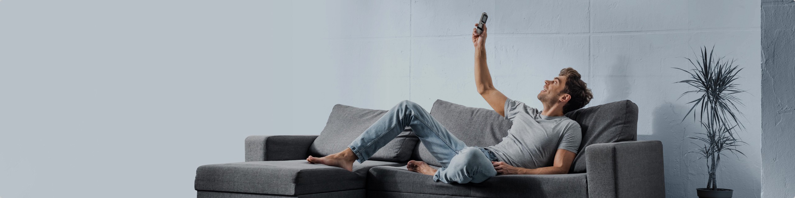 A man on his sofa setting the air conditioner with the remote