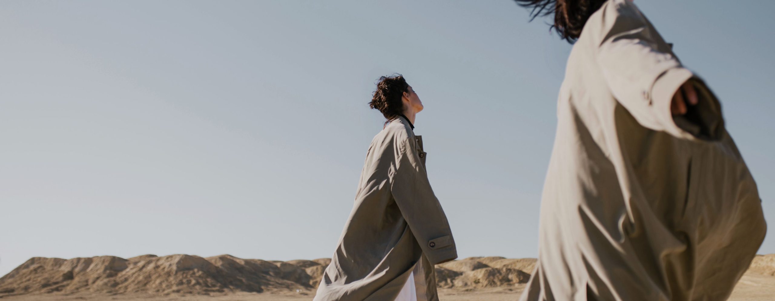 Two walkers in long coats crossing the dunes, from Salt Road