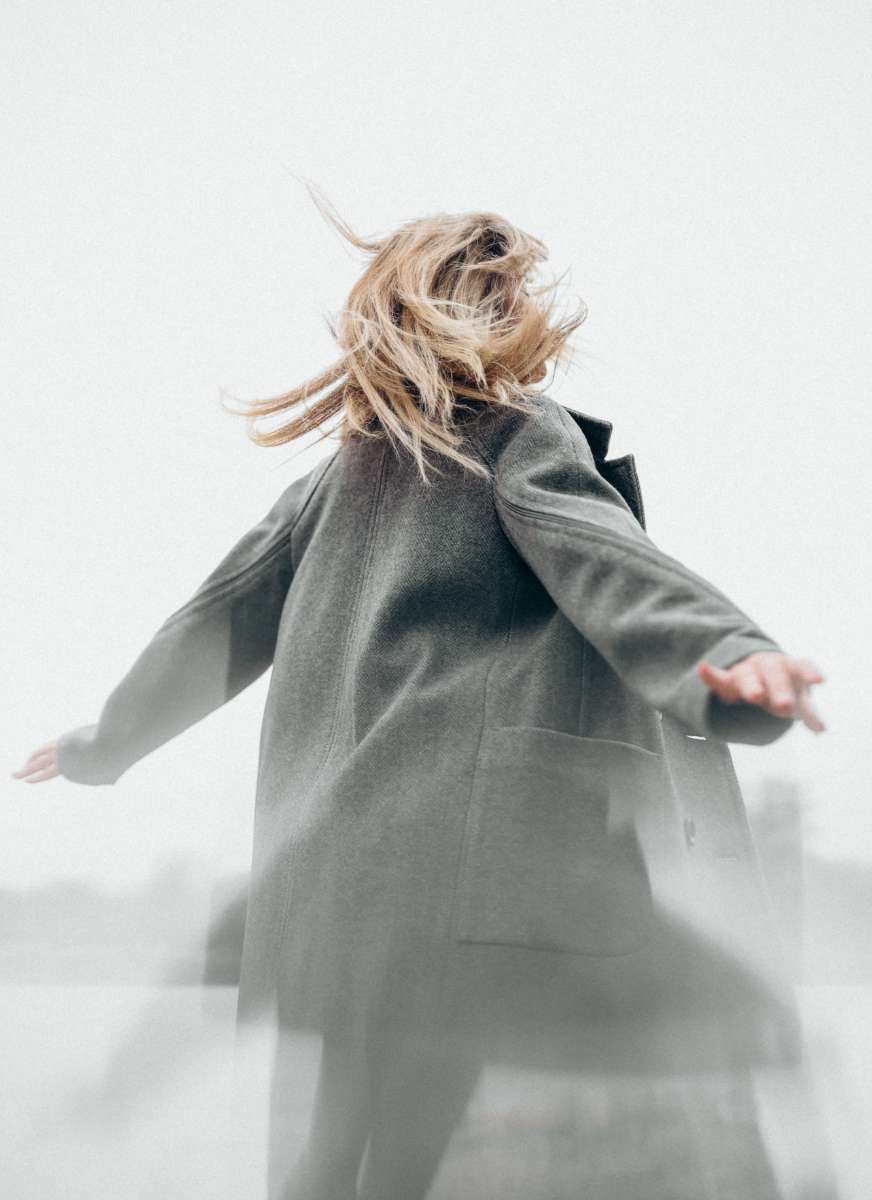 A woman turning in a long coat, from Weightless