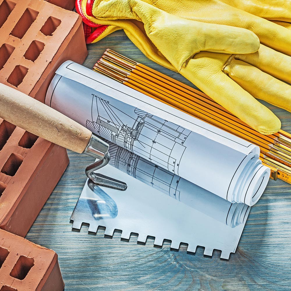 Plans, gloves and a trowel on a brick pile
