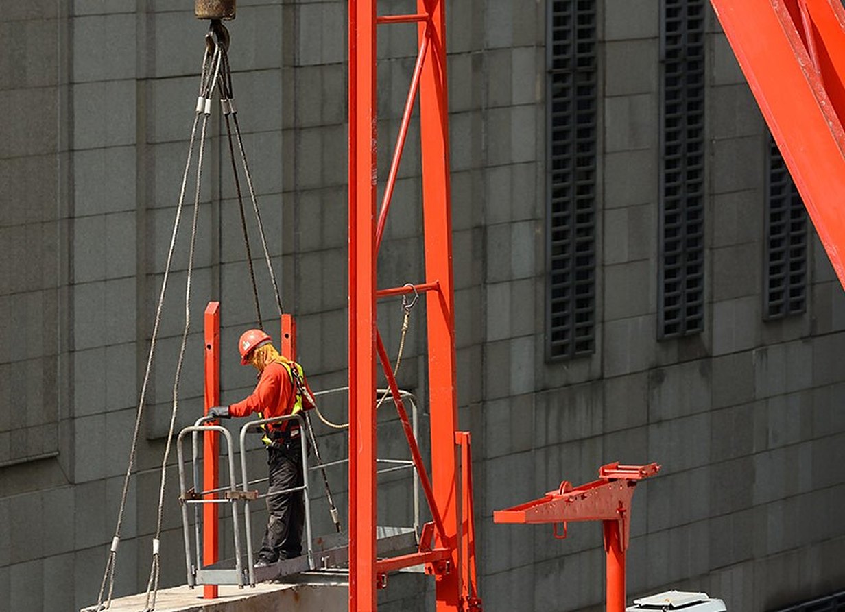 A worker in a basket on a red platform beside a power station
