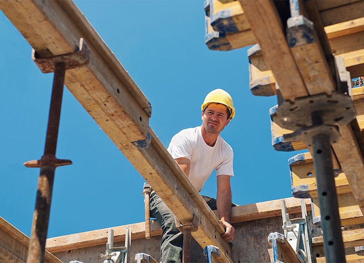 A carpenter on a timber house frame against a blue sky