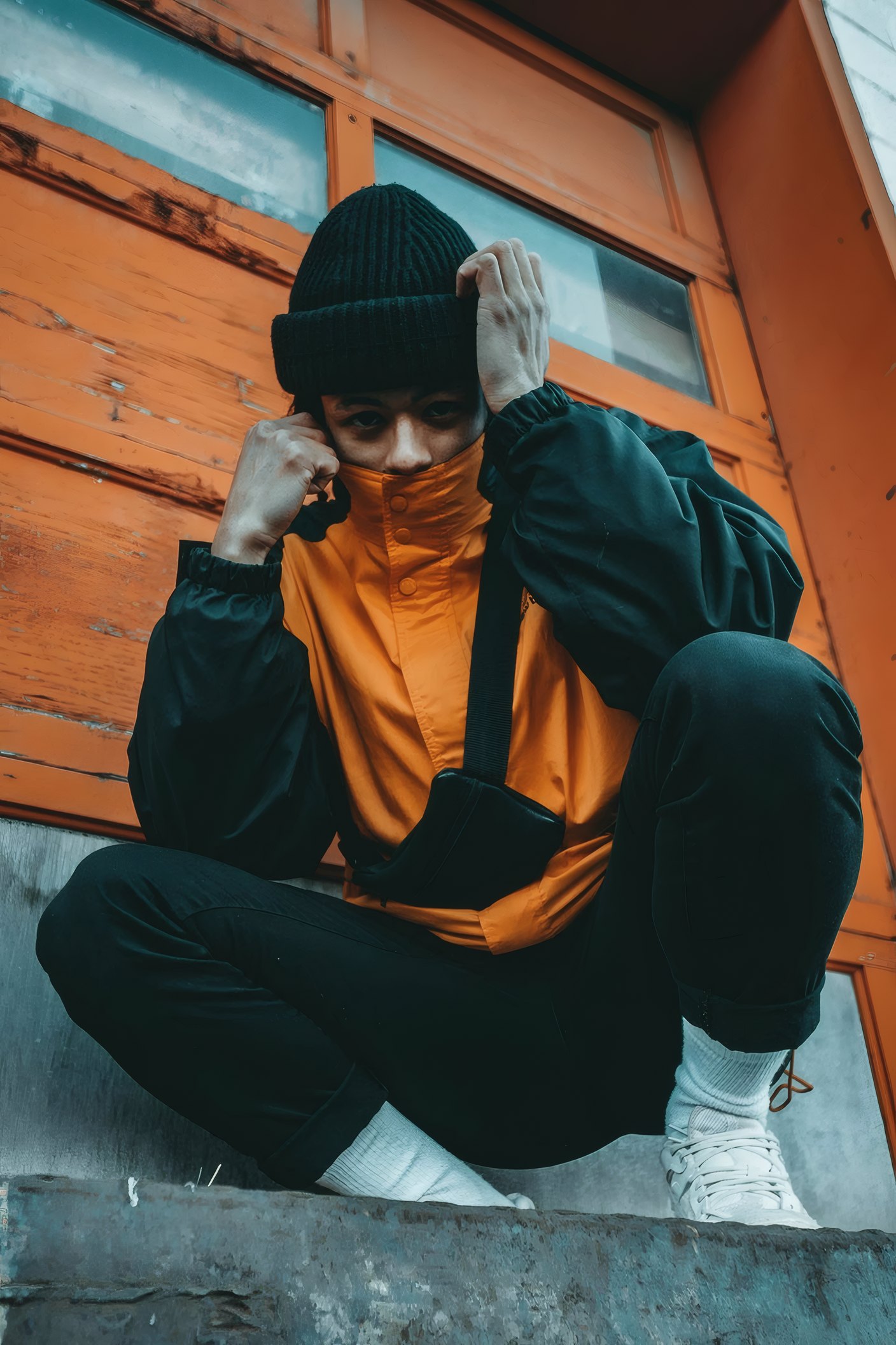 A skater in a beanie crouched on a ledge by an orange door