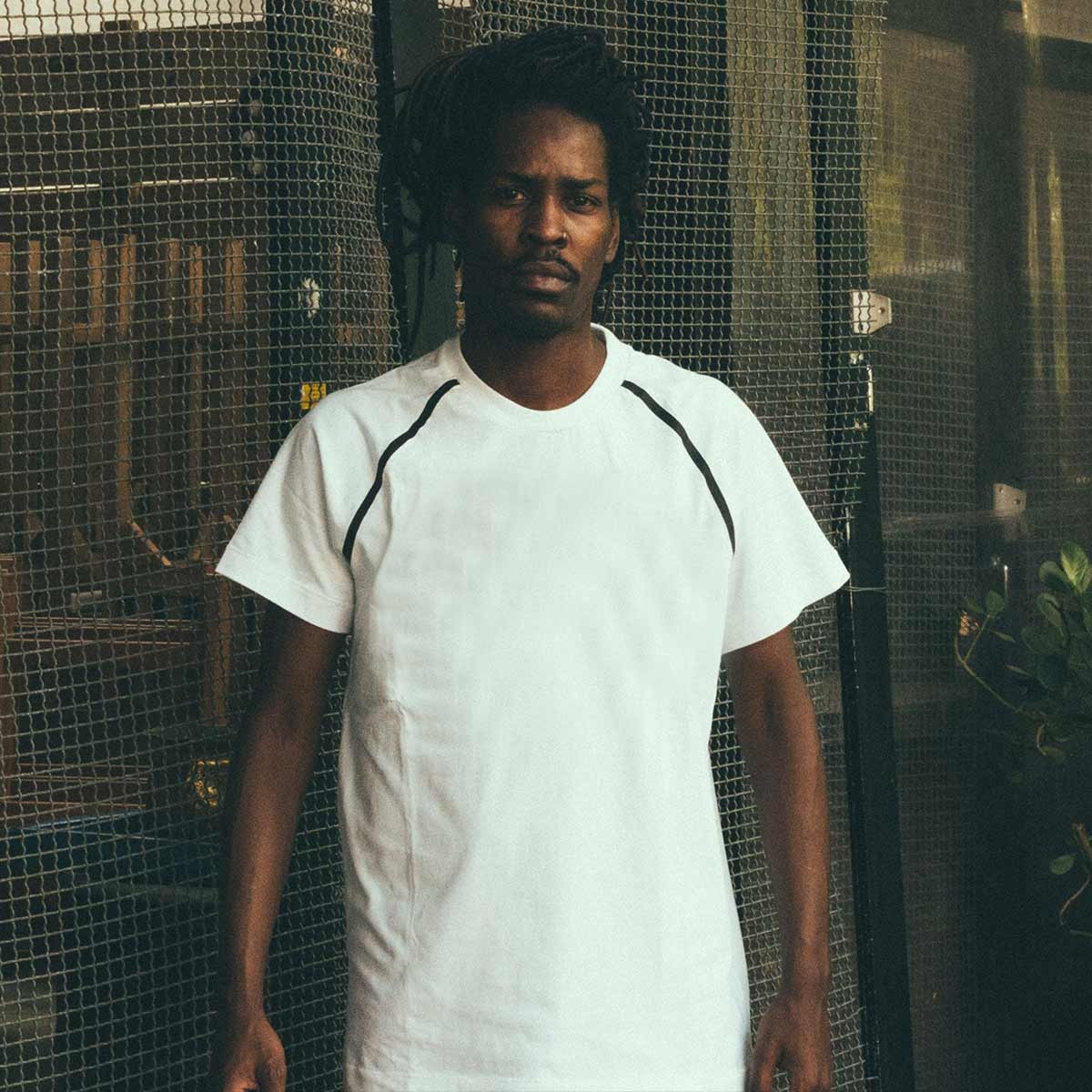 A man in a white tee against a mesh fence