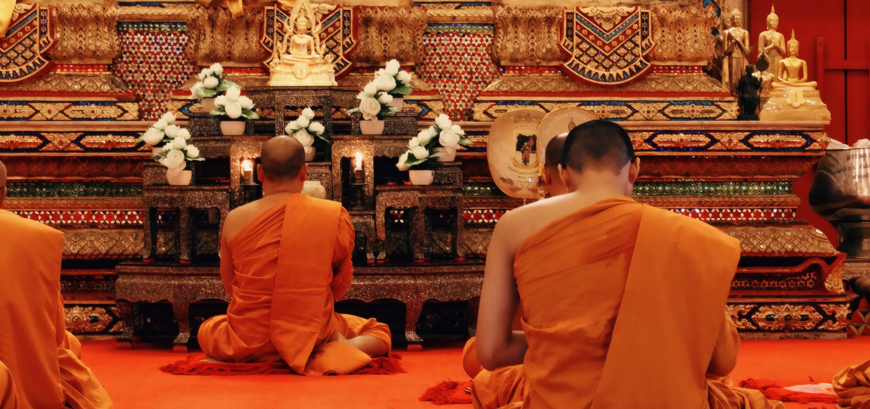 Monks in saffron robes praying before a golden shrine