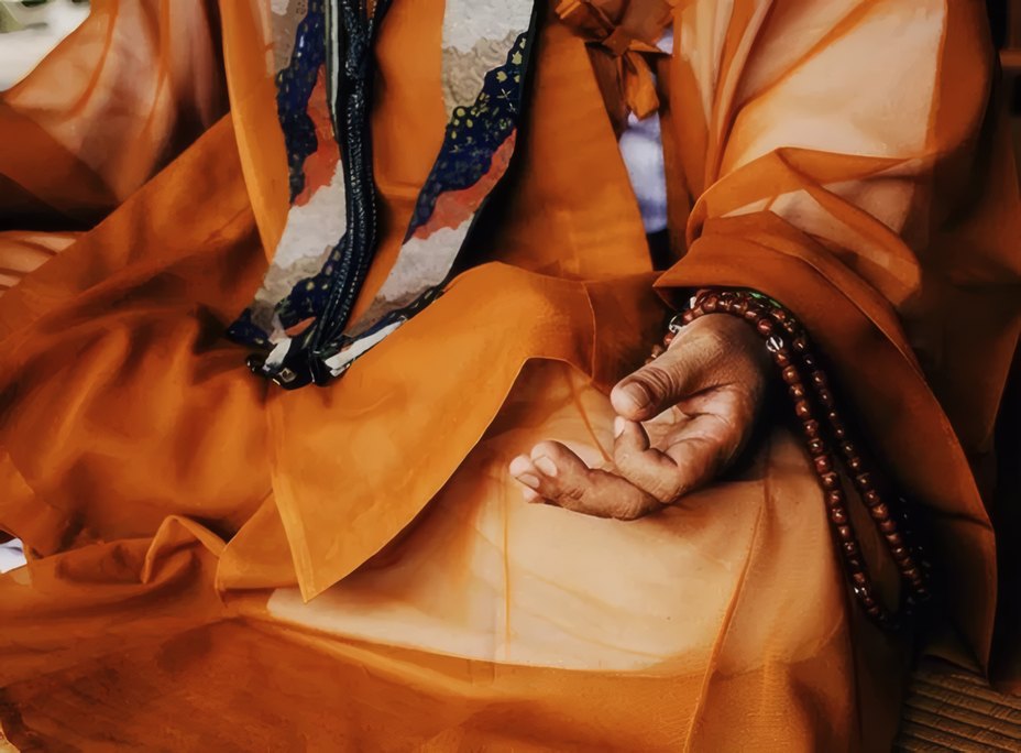 Hands holding prayer beads over saffron robes