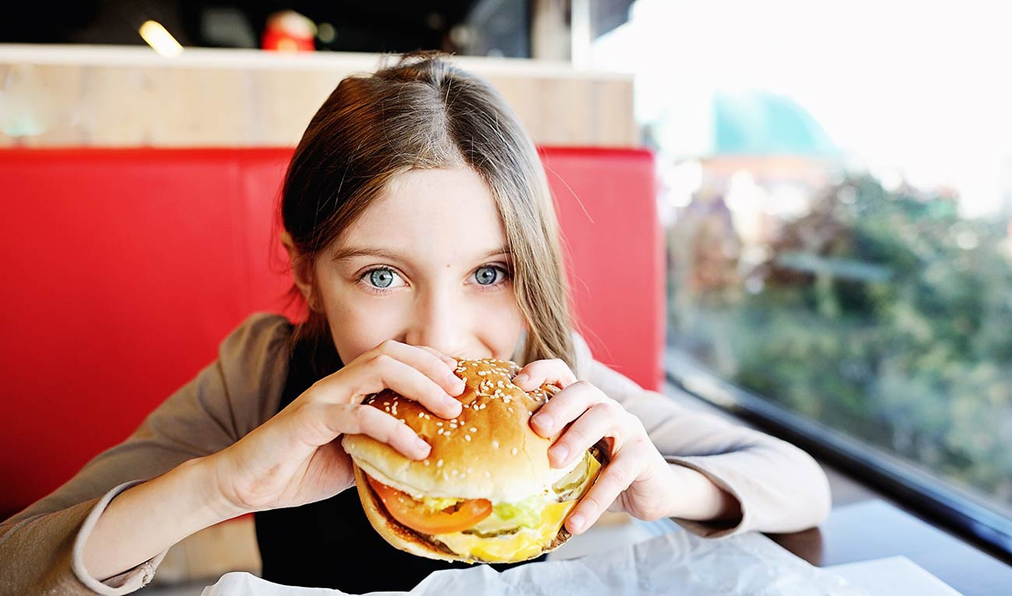 A girl biting into a burger in a red diner booth