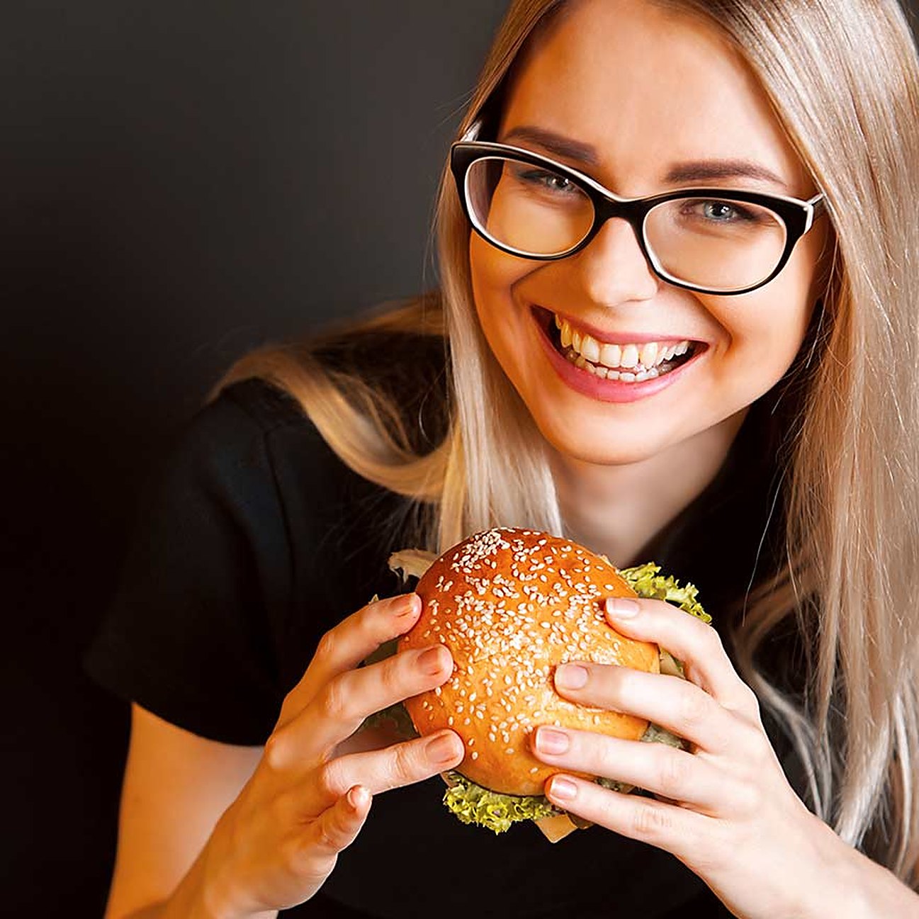 A laughing guest in glasses holding a burger