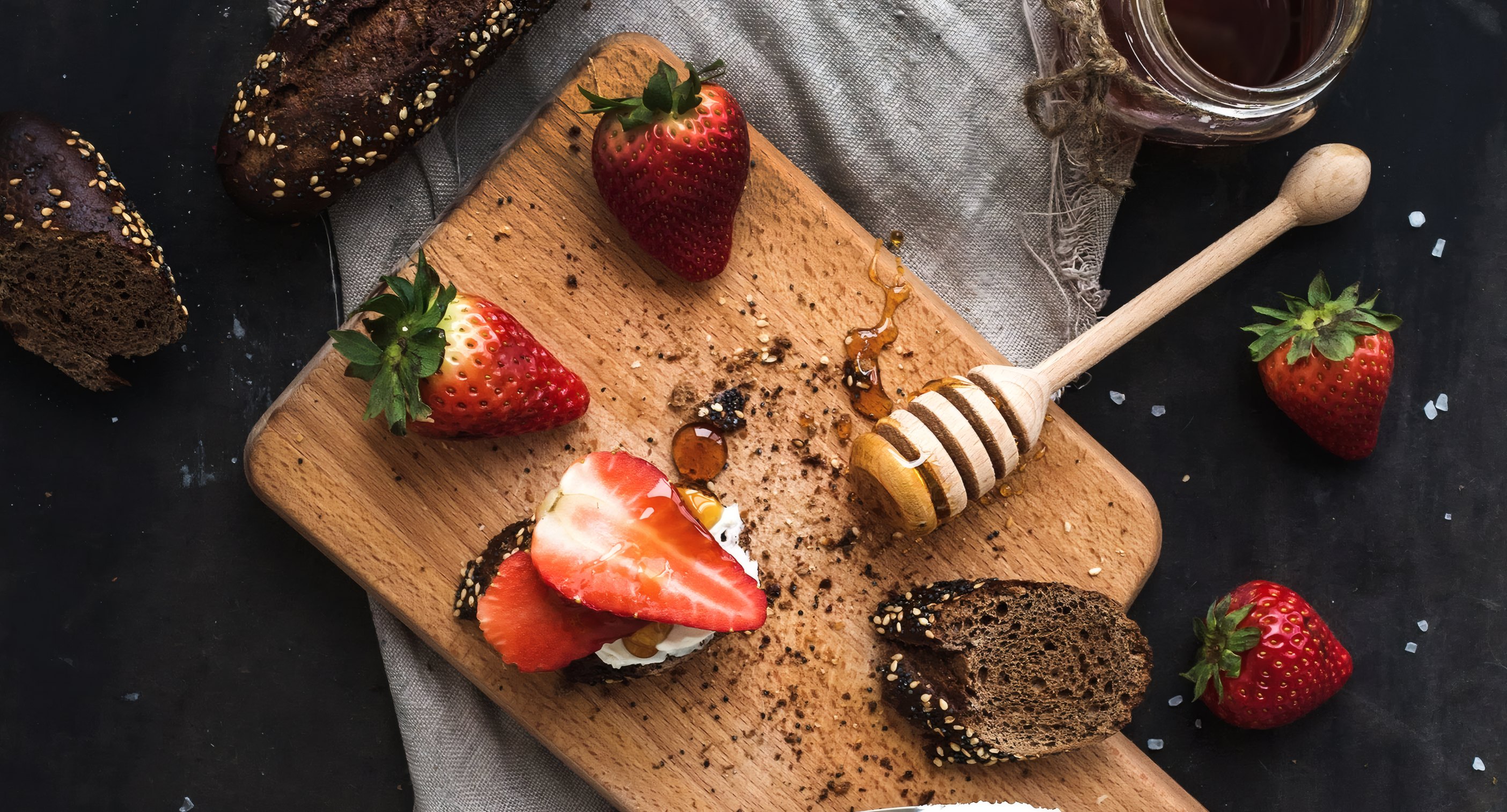 Strawberries, bread and honey on a dark board