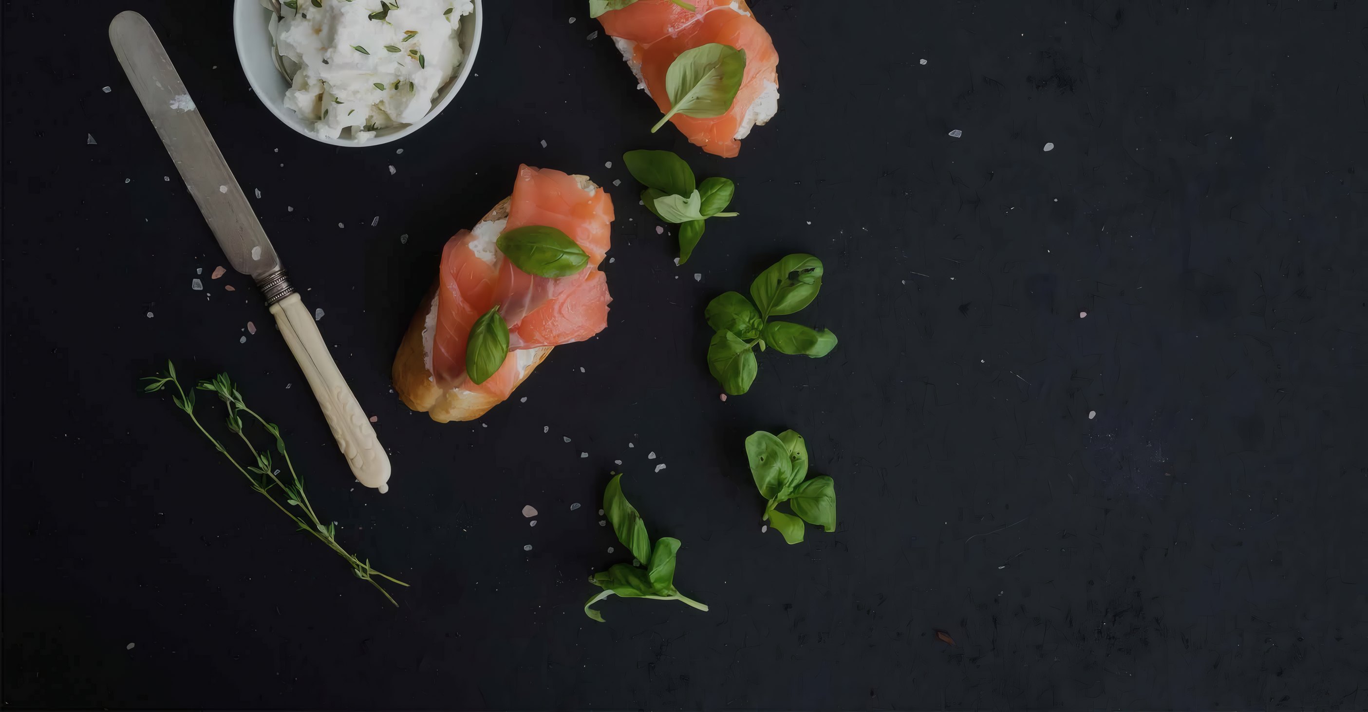 Smoked salmon, a knife and herbs on dark slate